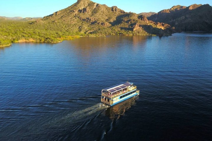 A small boat travels on a large, calm lake surrounded by mountains and greenery.