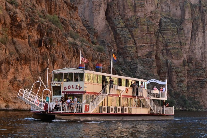 A vintage paddleboat named Dolly on a river with cliffs in the background.