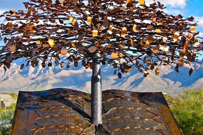 Metal tree sculpture emerging from open book with mountains in the background.